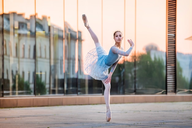 Young ballerina dancing on pointe shoes against the backdrop of the reflection of the sunset in the city