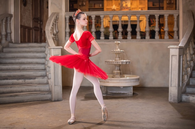 A young ballerina in a red tutu is dancing against the theatrical scenery of the palace.