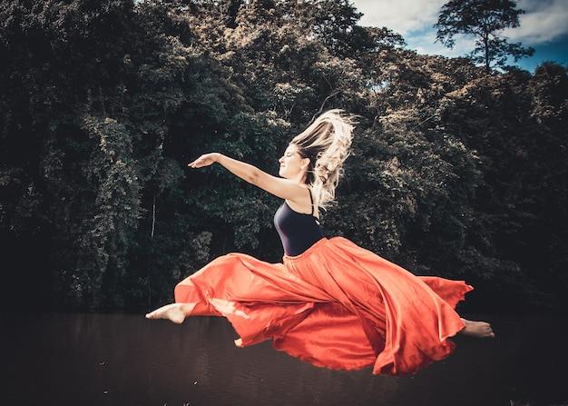 Молодая балетная танцовщица в красной юбке танцует в лесу