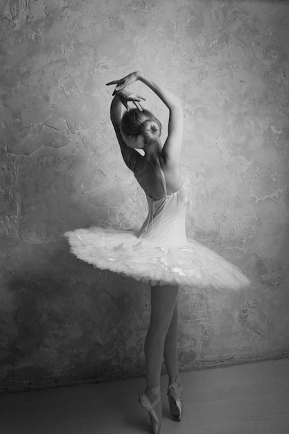 A young ballet dancer in a white tutu performing pointe work on the background of a textured wall