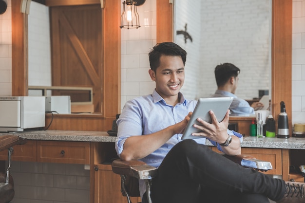 Young barber expert with tablet smiling in barber shop