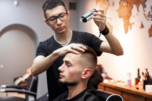 Young barber kazakh works in a barbershop handsome guy does hair styling for a client