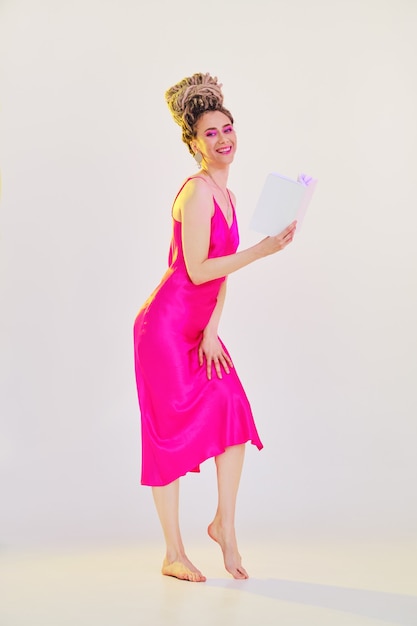 Молодая босиком женщина в розовом платье с шелковым ремешком держит открытую книгу