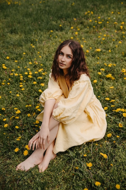 Young barefoot woman wearing a yellow dress sitting in a field with dandelions