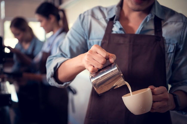 Foto giovane barista esperto nella preparazione di caffè campione che crea arte del latte in una tazza di caffè per un cliente