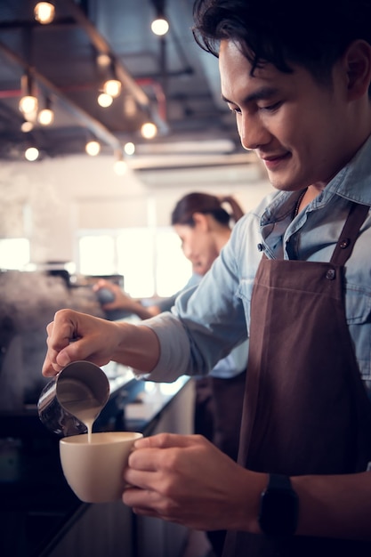사진 챔피언 커피를 만드는 데 능숙한 젊은 바리스타는 고객을 위해 커피 컵에 라테 아트를 만니다.