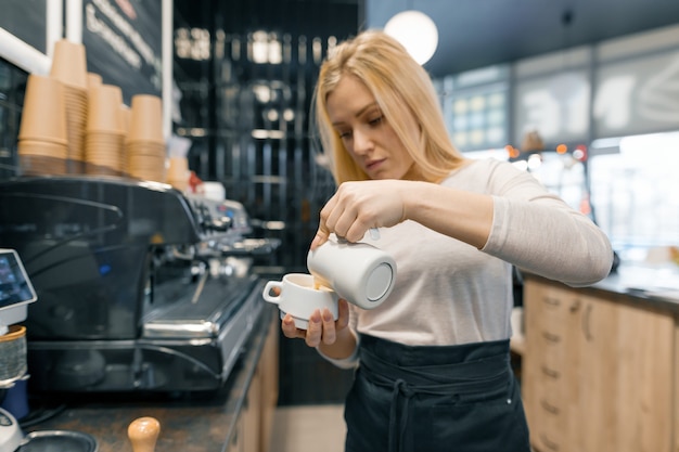 Il giovane barista che tiene il latte per prepara la tazza di caffè