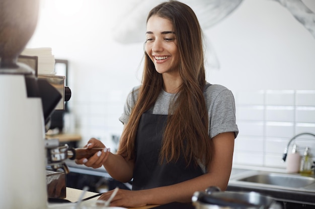 コーヒーグラインダーを使用して豆をポルタフィルターに粉砕する若いバリスタの学生