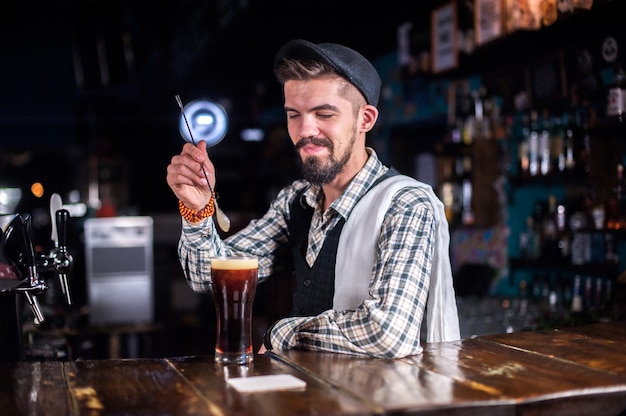 Young barman makes a cocktail while standing near the bar counter in bar