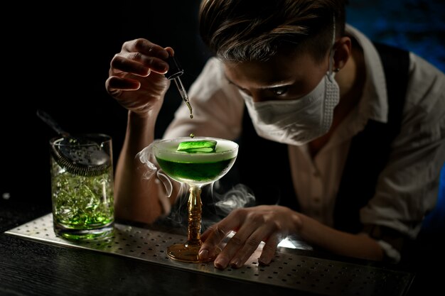 Young bartender carefully adds ingredient to glass with ice cocktail