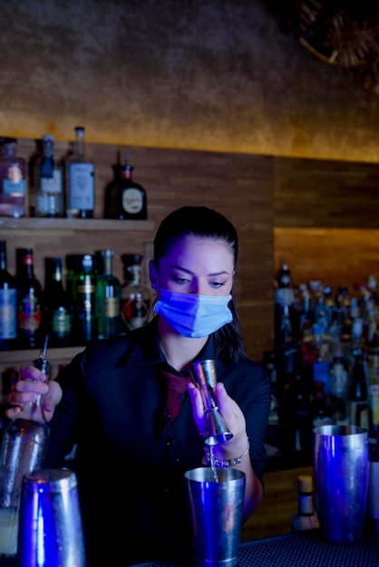 Young bartender girl with mask preparing cocktail on a bar counter. work concept