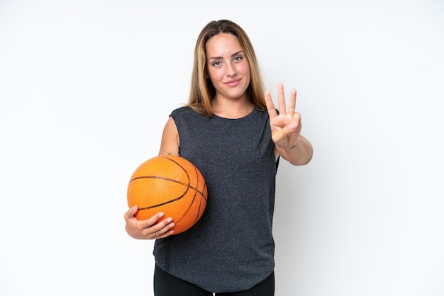 Giovane giocatore di pallacanestro donna caucasica isolata su sfondo bianco felice e contando tre con le dita