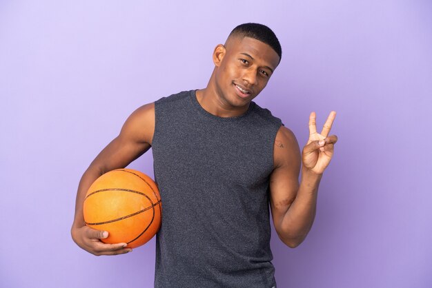 Uomo di giovane giocatore di basket latino isolato su viola sorridente e mostrando il segno di vittoria