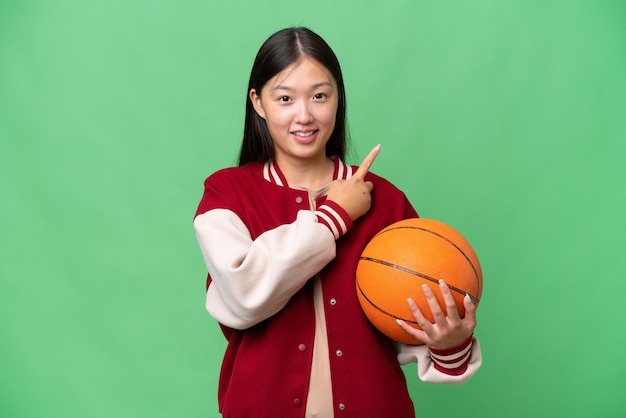 Young basketball player asian woman over isolated background pointing to the side to present a product