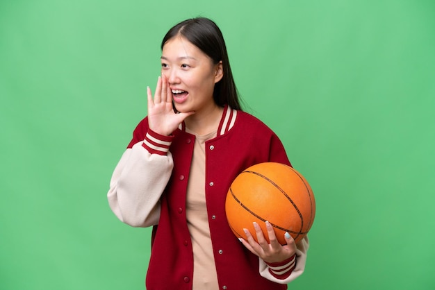 Young basketball player asian woman over isolated background shouting with mouth wide open to the side