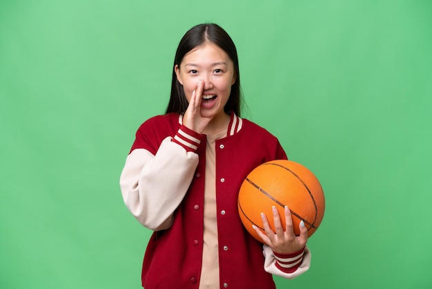 Giovane giocatore di basket donna asiatica su sfondo isolato gridando con la bocca spalancata