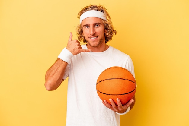 指で携帯電話の呼び出しジェスチャーを示す黄色の背景に分離された若いバスケットボール選手の白人男性。