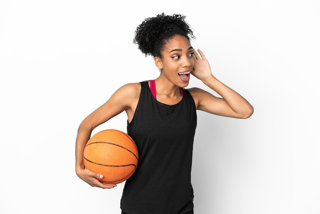 Young basketball player latin woman isolated on white background listening to something by putting hand on the ear