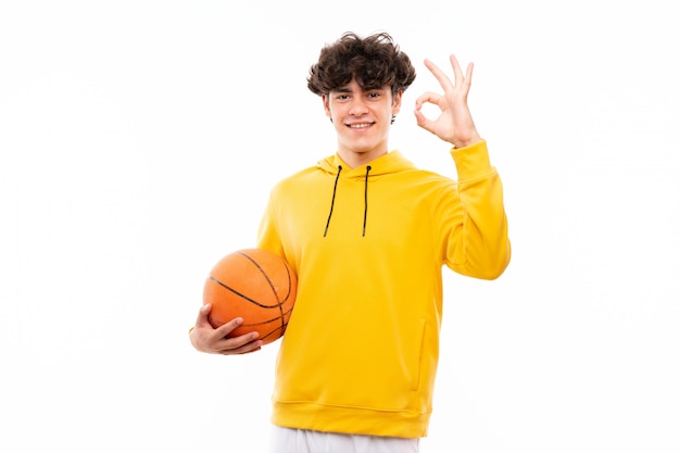 Young basketball player man over isolated white wall showing ok sign with fingers