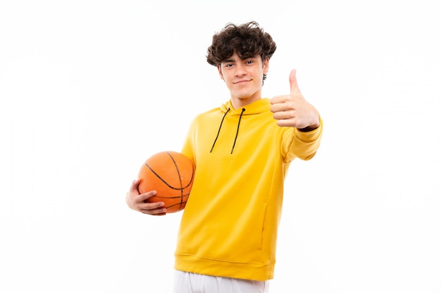 Молодой баскетболист человек над белой стене с большими пальцами руки вверх, потому что случилось что-то хорошее