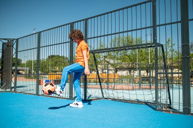 Young basketball player standing at the gate while kicking the\
ball with his left foot