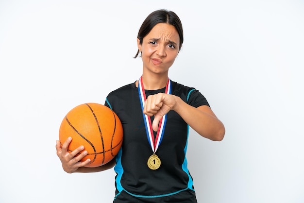 부정적인 표정으로 엄지손가락을 보여주는 흰색 배경에 고립 된 젊은 농구 선수 여자
