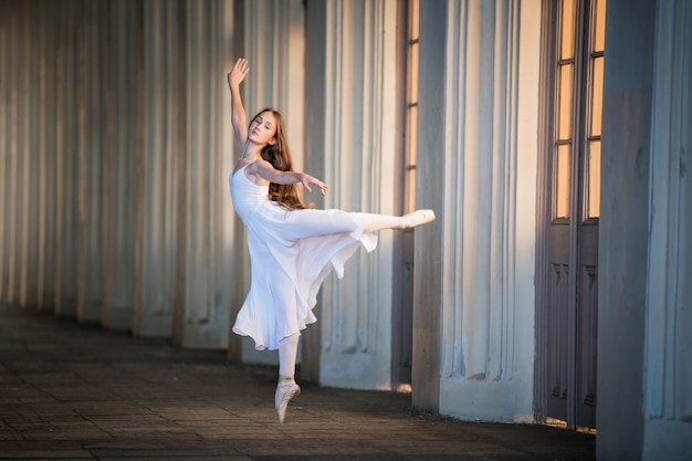 Young bayerina in a long white skirt with long loose hair stands in a graceful pose on pointes