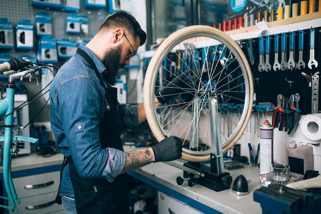 Young beard bicycle mechanic repairing bicycles in a workshop.