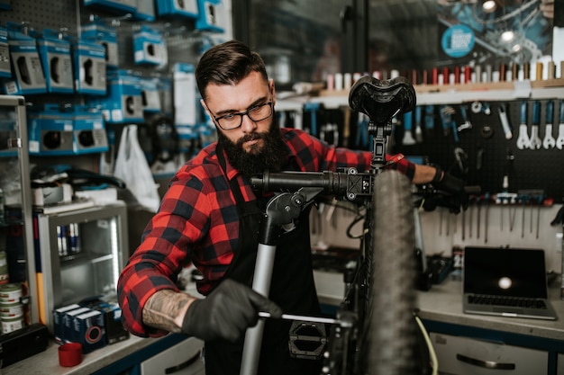 Young beard bicycle mechanic repairing bicycles in a workshop.