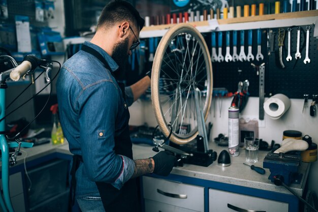 Young beard bicycle mechanic repairing bicycles in a workshop.