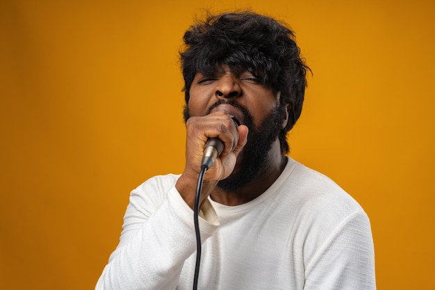 Photo young bearded african american man singing in microphone against yellow background
