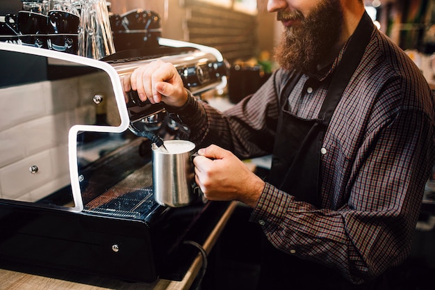 Giovane barista barbuto che galleggia latte