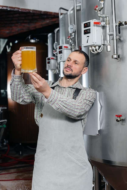 Foto un giovane birraio barbuto effettua il controllo di qualità della birra appena prodotta nel birrificio.