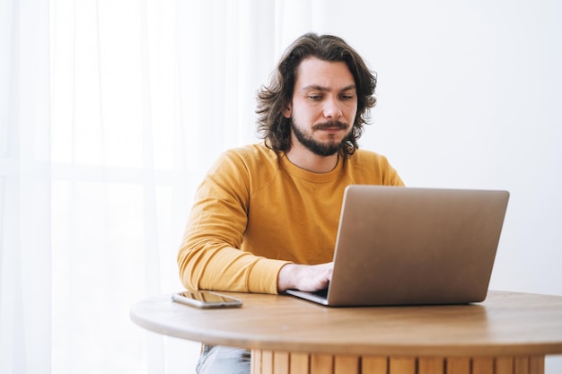 Young bearded brunette business man in casual yellow longsleeve working on laptop in the modern office