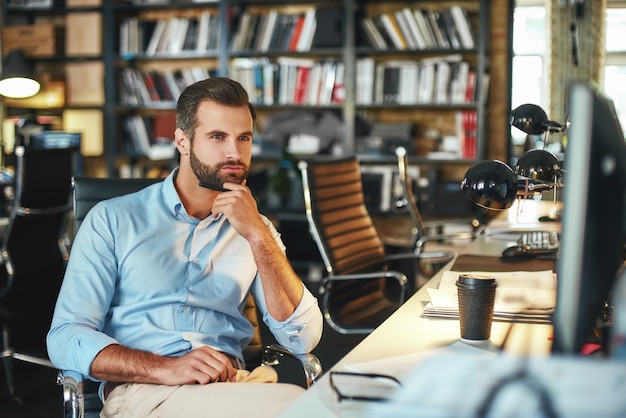 Young bearded businessman in formal wear touching his chin and thinking about something 