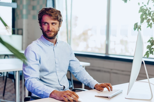 Young bearded businessman using his computer in a modern office place. Business concept