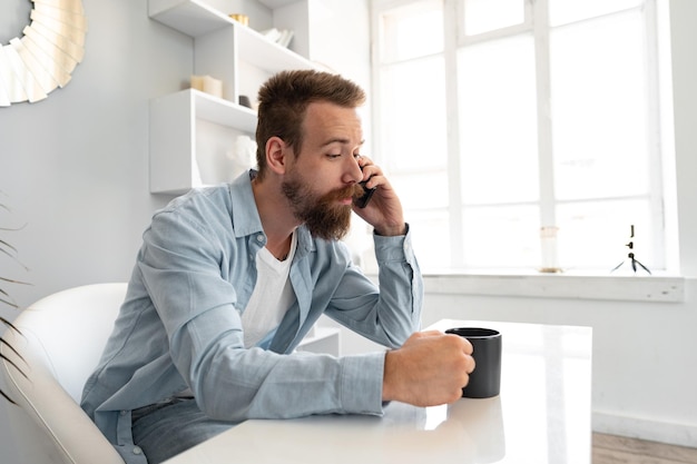 机に座って携帯電話で話している自宅で働く若いひげを生やしたビジネスマン