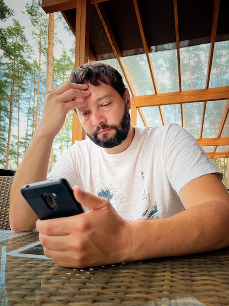 Young bearded caucasian man using smartphone sitting on terrace