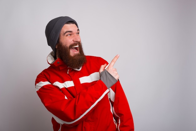 Young bearded climber is being excited an is pointing at copy space near a white wall.