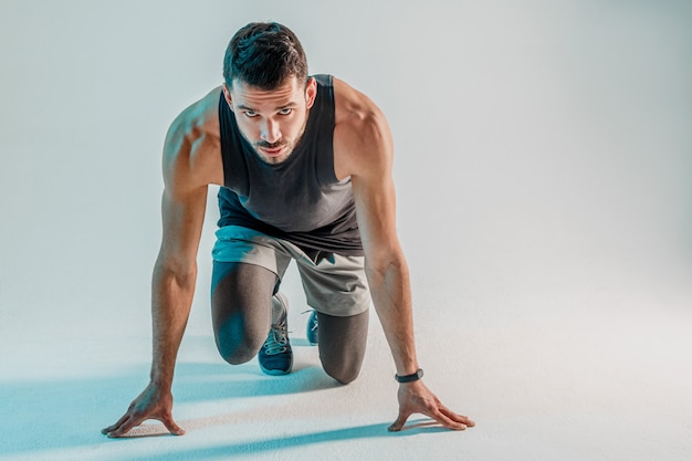 Young bearded concentrated european runner on start. Sportsman wear sports uniform and looking at camera. Isolated on turquoise background. Studio shoot. Copy space