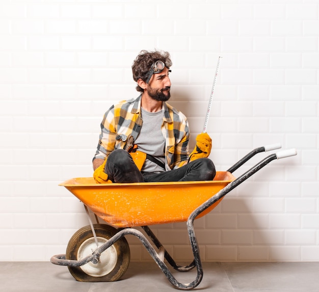 Young bearded construction worker man on a wheelbarrow