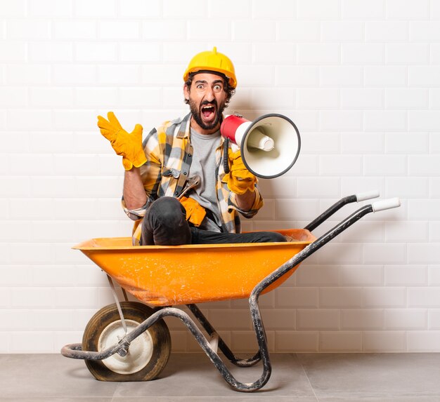 Young bearded construction worker man on a wheelbarrow