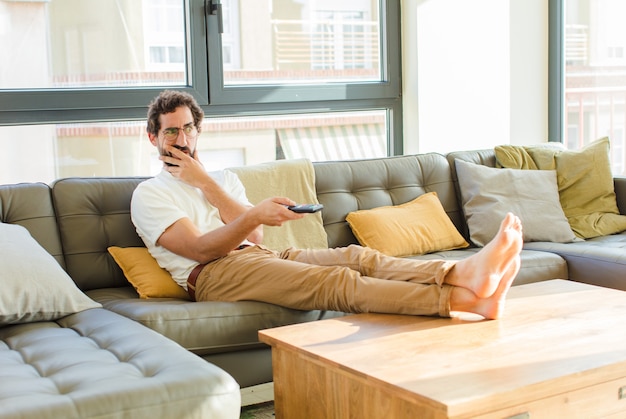 Молодой бородатый крутой мужчина сидит на диване у себя дома