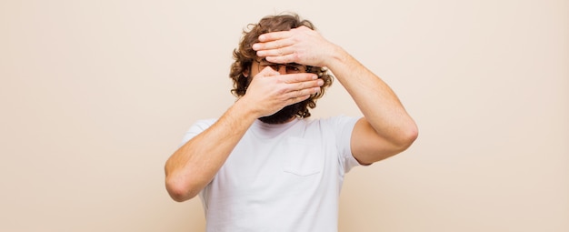 Photo young bearded crazy man covering face with both hands saying no to the camera! refusing pictures or forbidding photos against pink wall