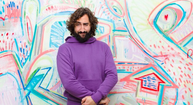 Young bearded crazy man looking proud, confident, cool, cheeky and arrogant, smiling, feeling successful against graffiti wall