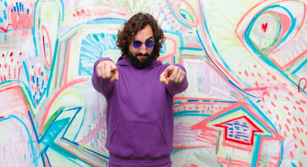 Young bearded crazy man pointing forward  with both fingers and angry expression, telling you to do your duty against graffiti 