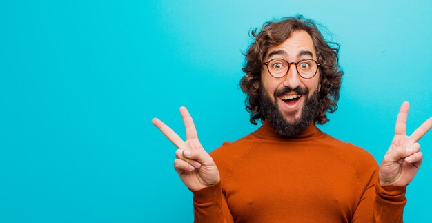 Young bearded crazy man smiling and looking happy, friendly and satisfied, gesturing victory or peace with both hands