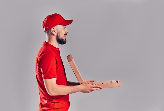 Photo young bearded delivery man with pizza box isolated on gray background. side view.