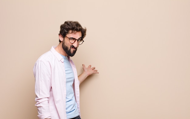 Young bearded expressing a concept against flat wall