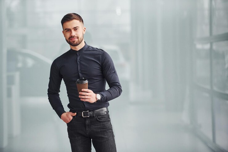 Photo young bearded guy in elegant clothes standing indoors against grey background.